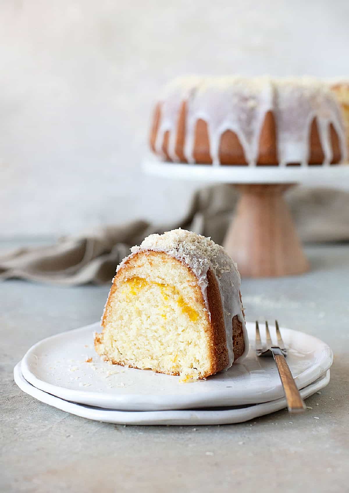 Glazed mango coconut bundt cake on a white plate. Cake stand in the grey background. Grey surface.