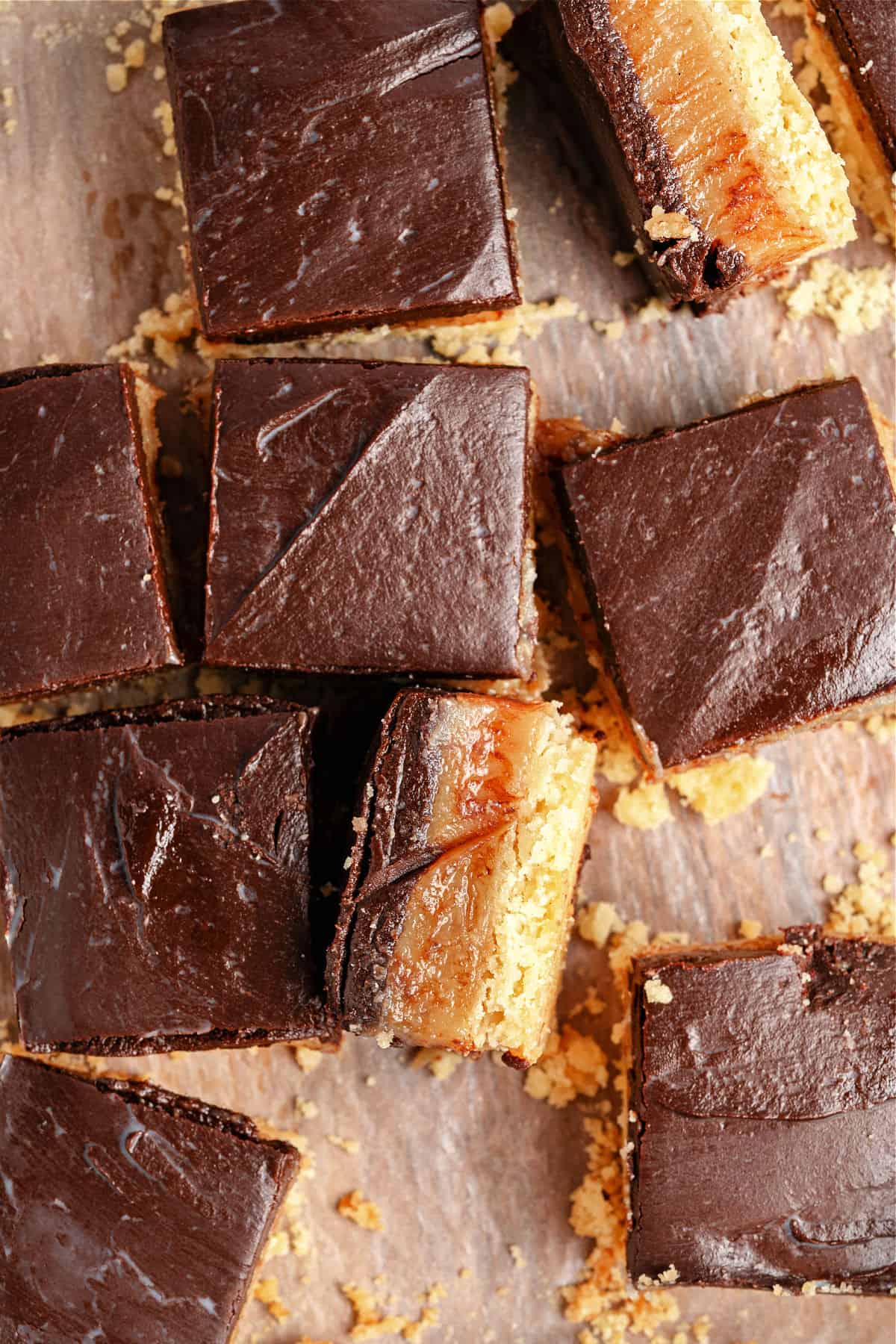 Top view of chocolate-topped caramel bar squares. Wooden surface.