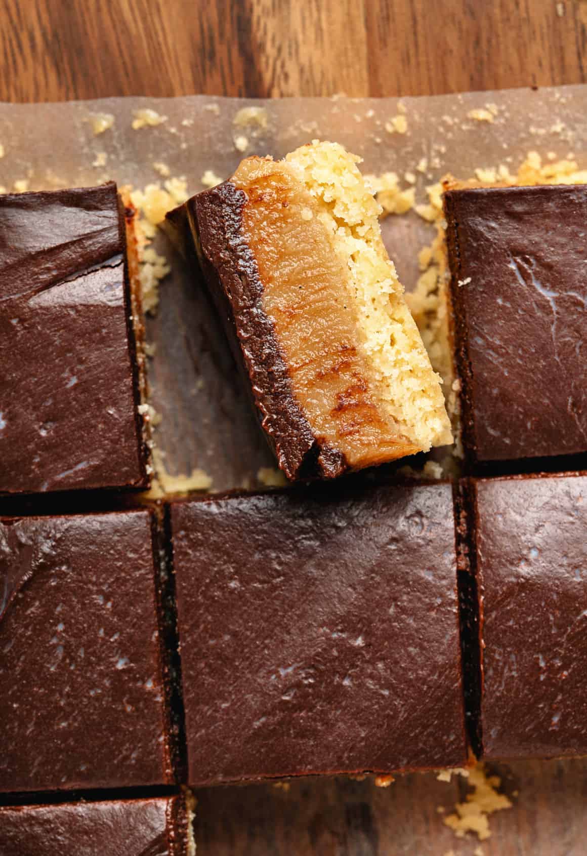 Caramel millionaire bar on the side among chocolate-topped squares. Wooden surface. Top view.