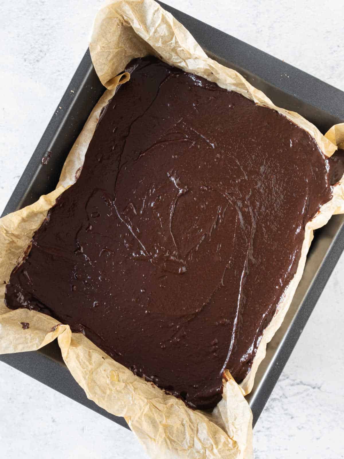 Chocolate layer on a metal square pan with parchment paper. Whitish surface.