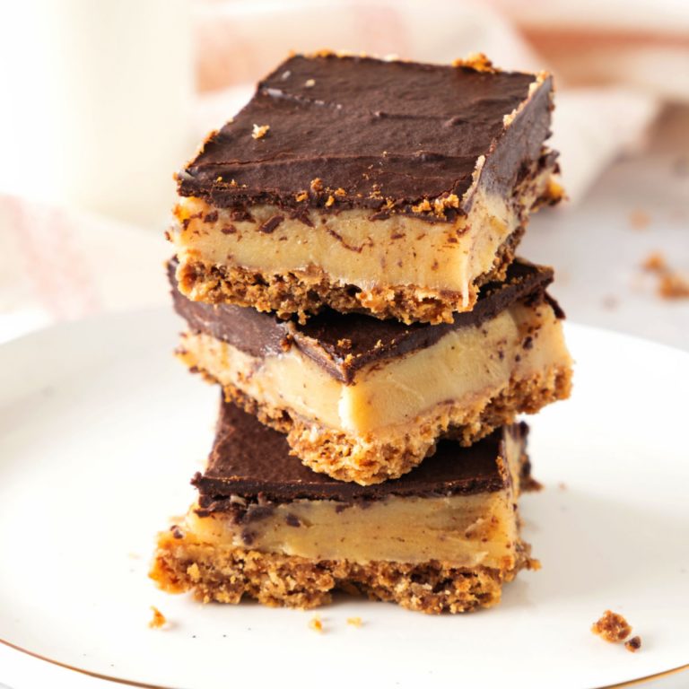 Stack of three millionaire shortbread bars on a white plate with a light pink cloth in the background.