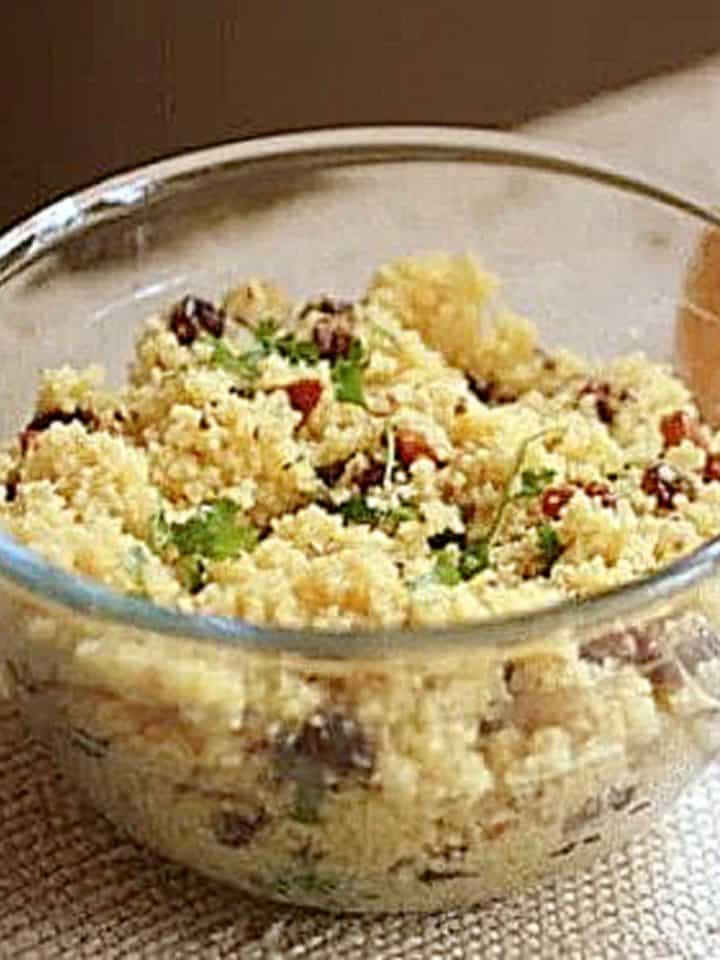 A glass bowl with raisin couscous on a beige cloth.