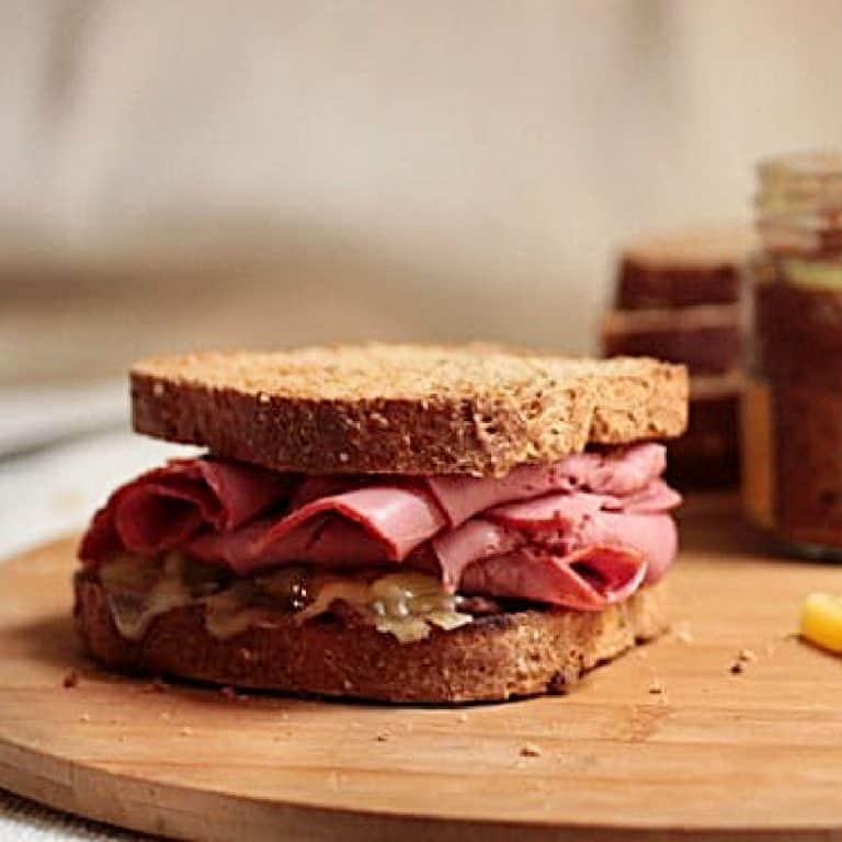 Pastrami sandwich on a wooden board with a mustard jar.
