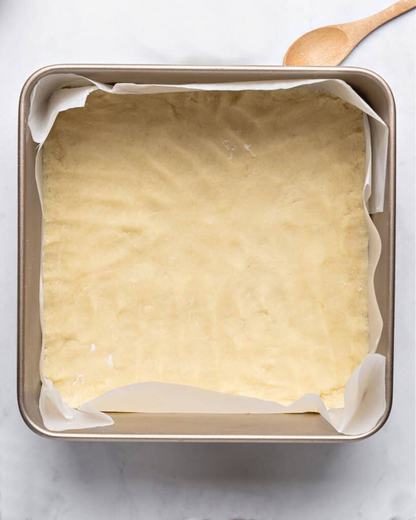 Shortbread crust patted on a parchment-lined metal pan. Top view. 