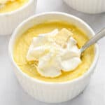 Close up white chocolate custard with cream dollop in a white ramekin. Light gray surface.