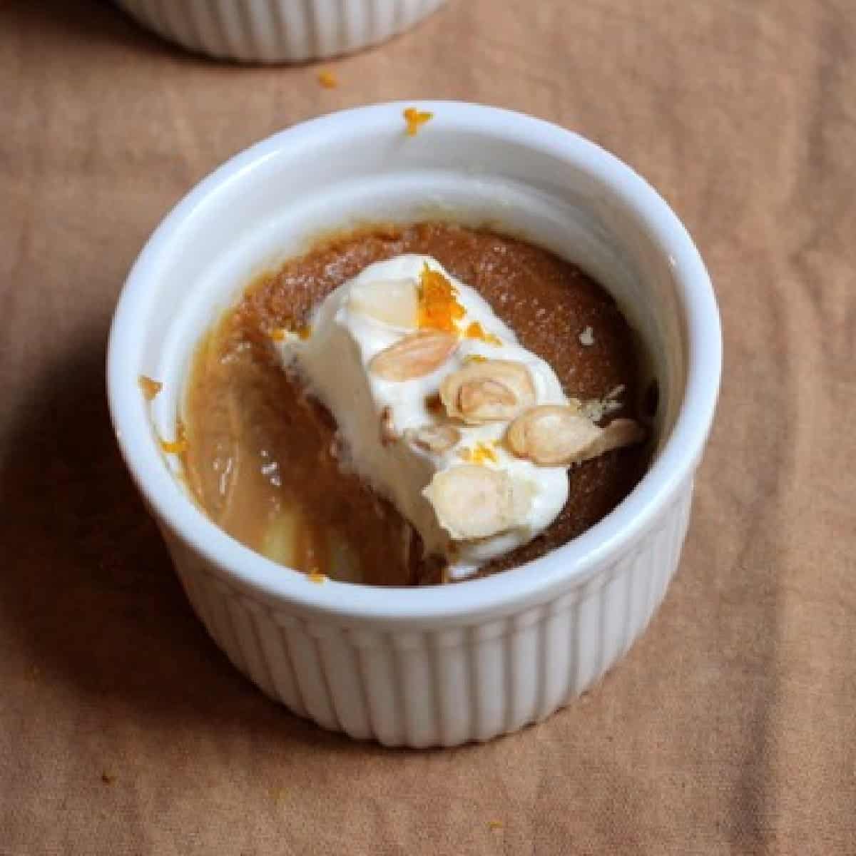 Eaten caramel white chocolate custard with cream on a white ramekin on a brown cloth.