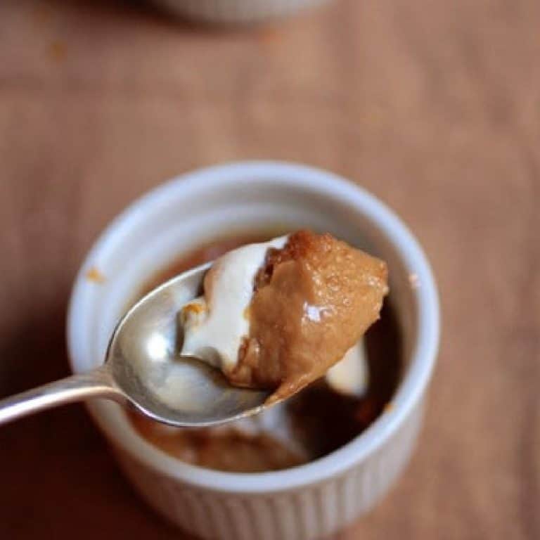 Silver spoon with bite of white chocolate cream custard. White ramekin below on a brown surface.