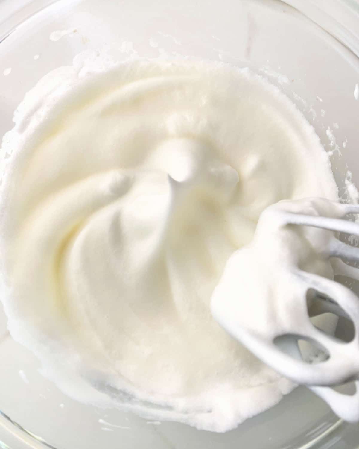 Egg whites beaten to stiff peaks with an electric mixer in a glass bowl. White surface.