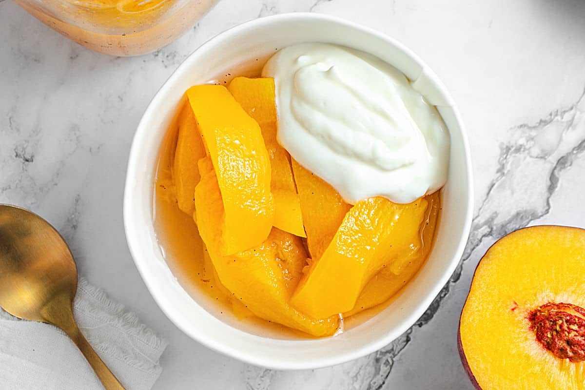 Serving of vanilla syrup peaches with yogurt in a white bowl. Marble surface. Top view.