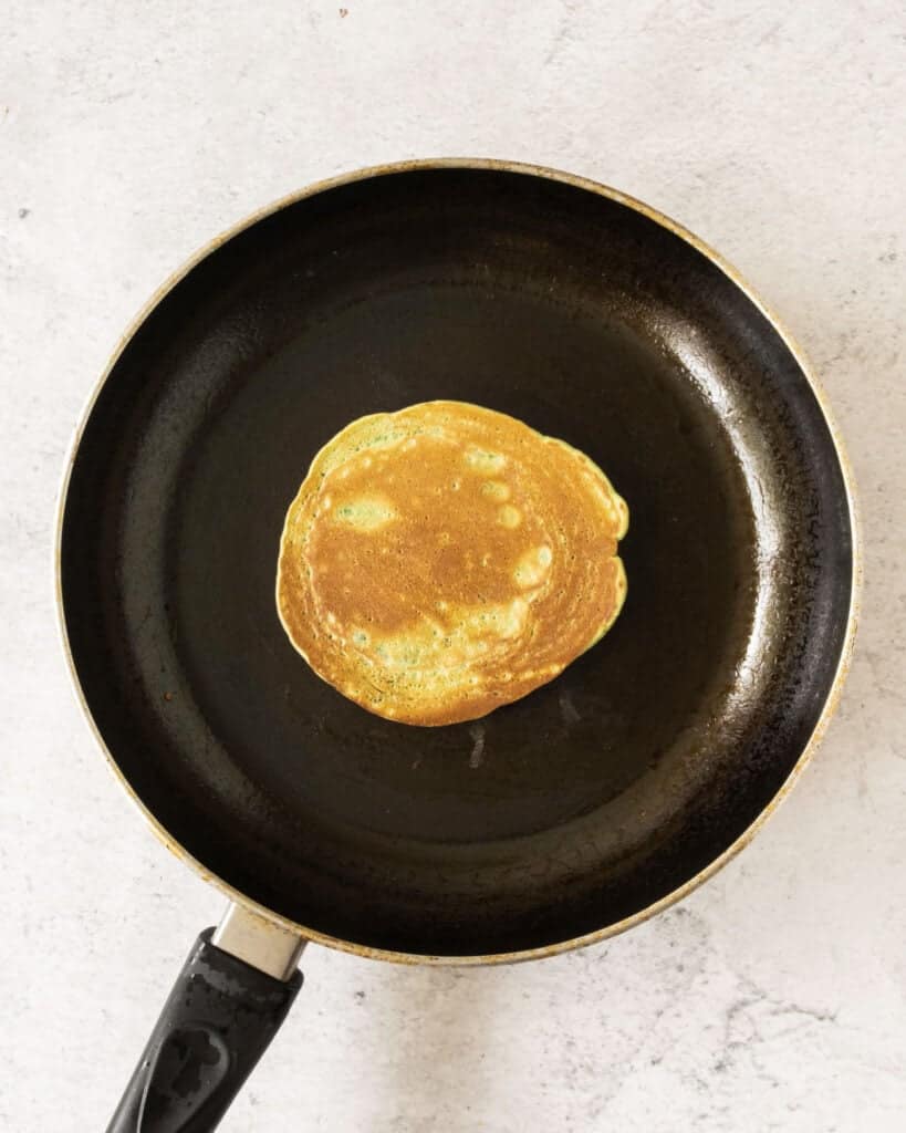 Cooking pancakes on a black skillet. Top view, stone background.