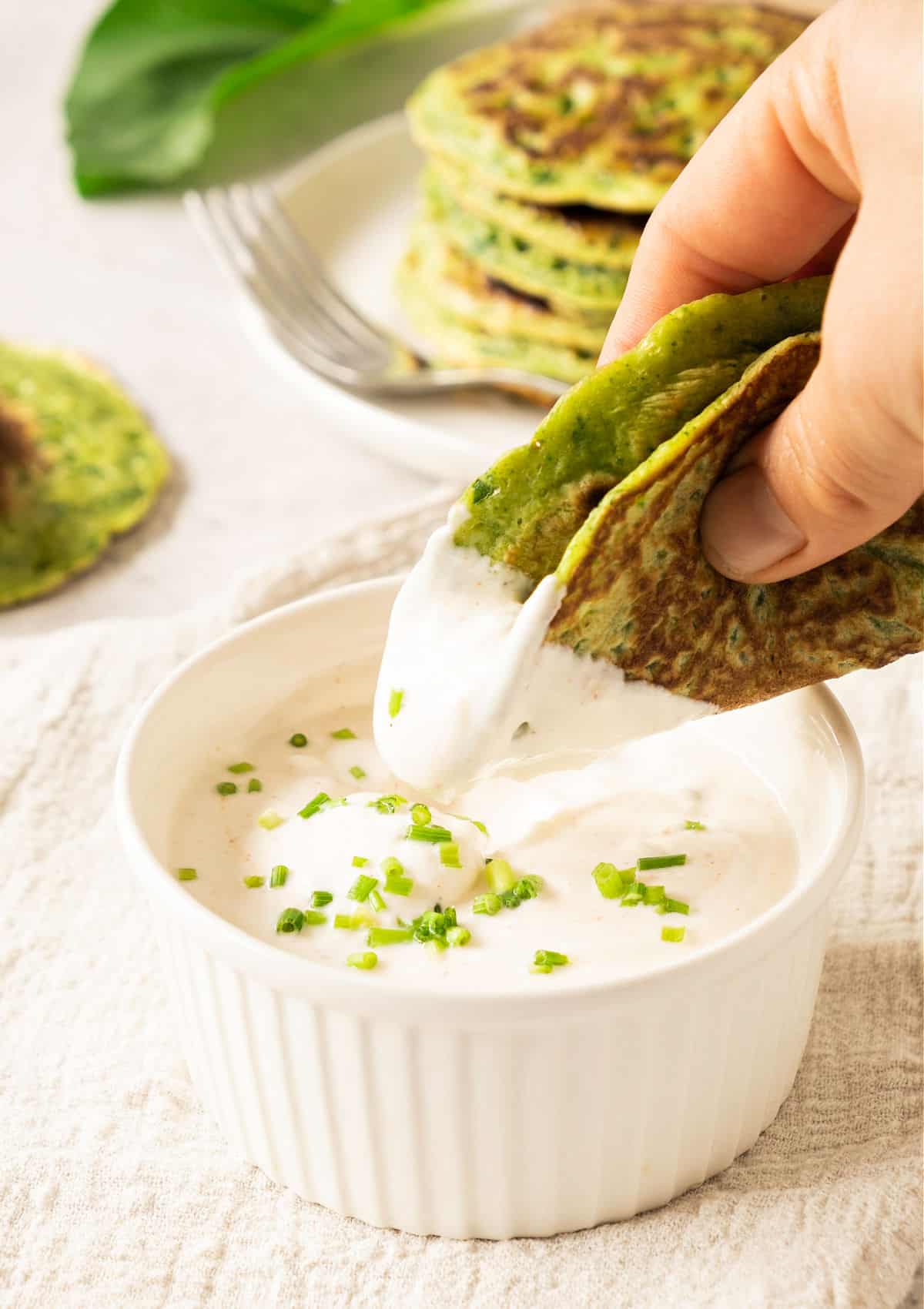 Folded chard pancake dipped in sour cream in a white bowl.