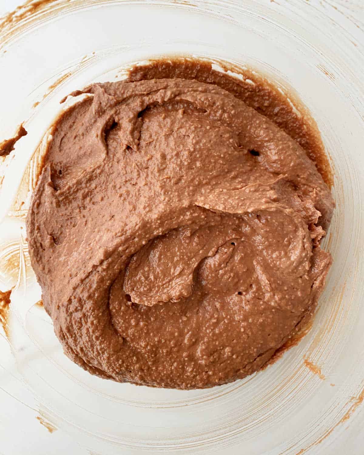 Almond chocolate cake batter in a glass bowl on a white surface. Close up image.