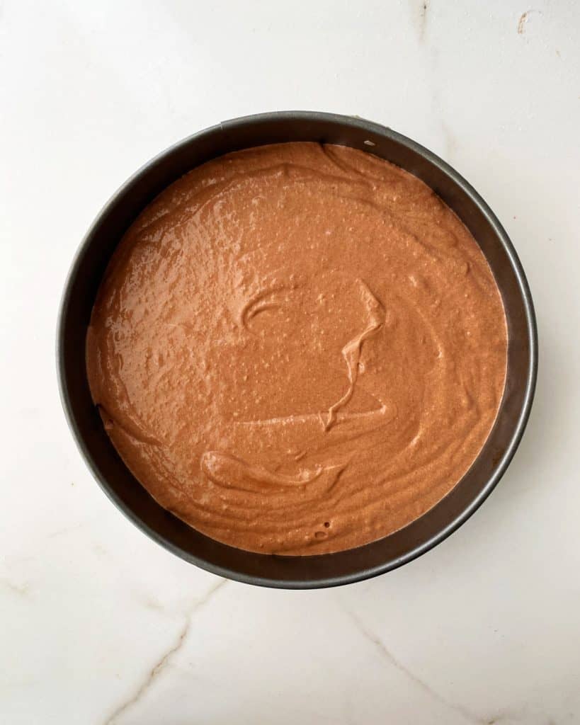 Top view of round cake pan with chocolate batter. White marble surface.