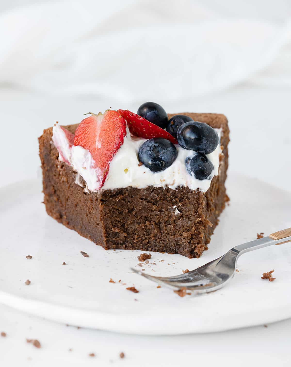 Eaten slice of chocolate cake with cream and berries on a white plate. Silver fork. White background.
