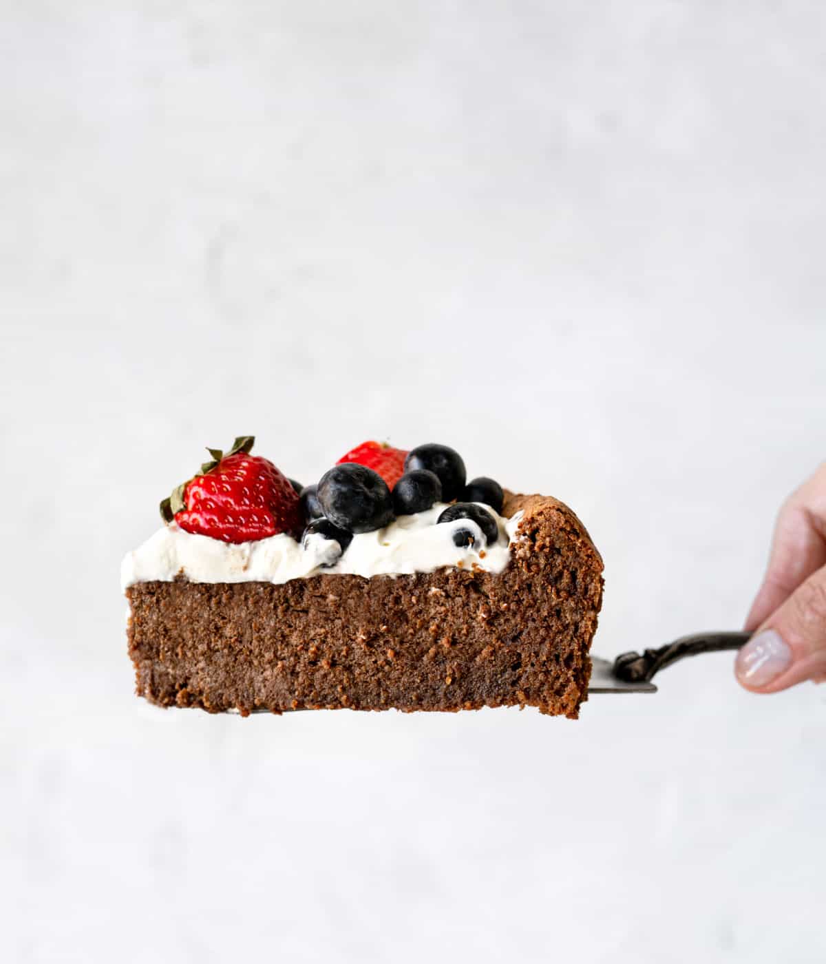 Single slice of cream and berry covered chocolate torte on a cake serves. Grey background. 