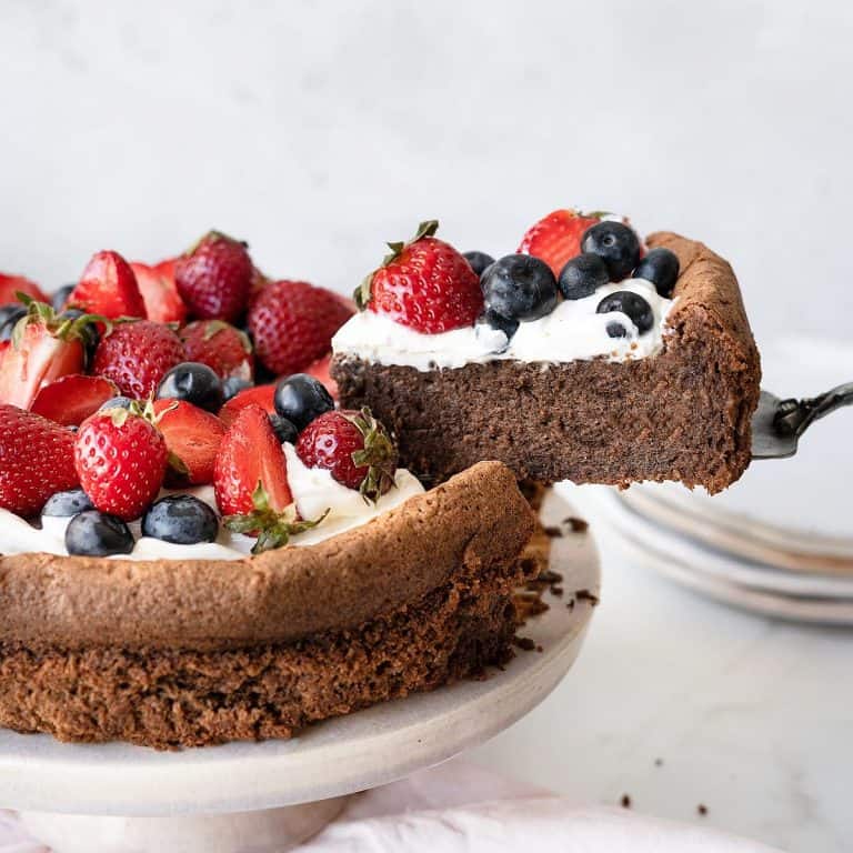 A berry topped chocolate torte on a pink cake stand with one slice being removed. Grey and white background.