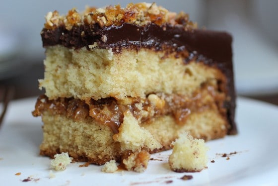 Close up of eaten slice of chocolate covered dulce de leche cake on a white plate.