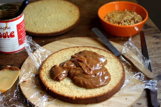 Filling a vanilla cake layer with dulce de leche on a wooden board.