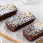 Three rectangular chocolate financiers with powdered sugar on a white paper.
