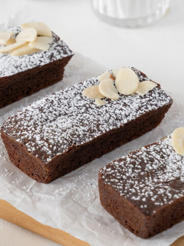 Three rectangular chocolate financiers with powdered sugar on a white paper.