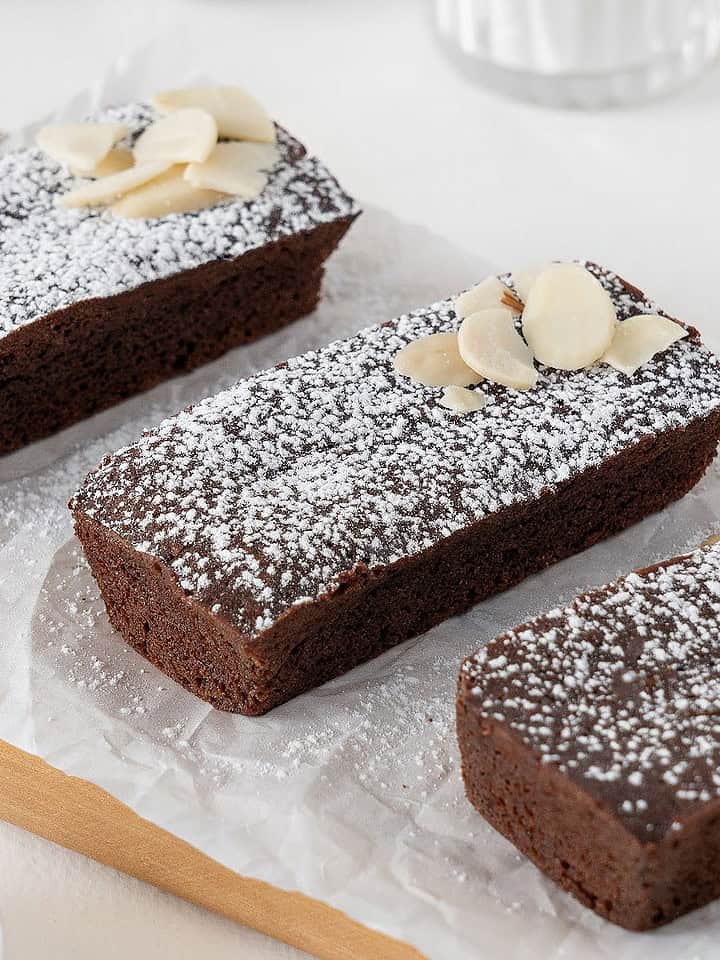 Three rectangular chocolate financiers with powdered sugar on a white paper.