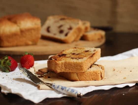 Slices of loaf bread on napkins, a butter knife, strawberries and loaf in the background.