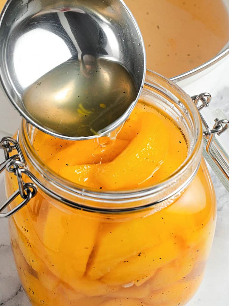 Pouring syrup into a mason jar with peach slices.