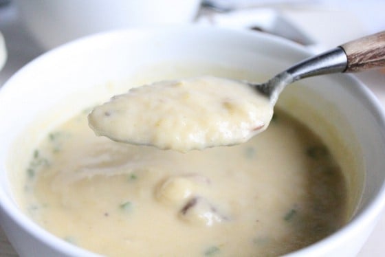 Spoon with soup over white bowl with potato soup. 