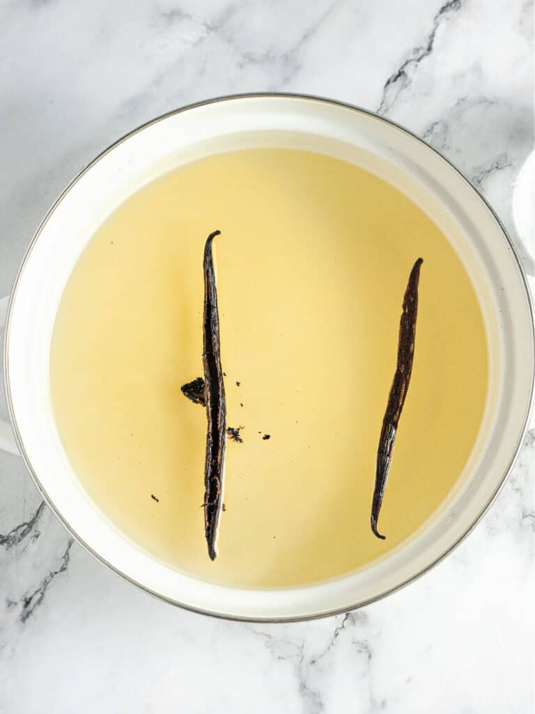 Sugar syrup with vanilla beans in a white saucepan. Top view. Gray marbled surface.