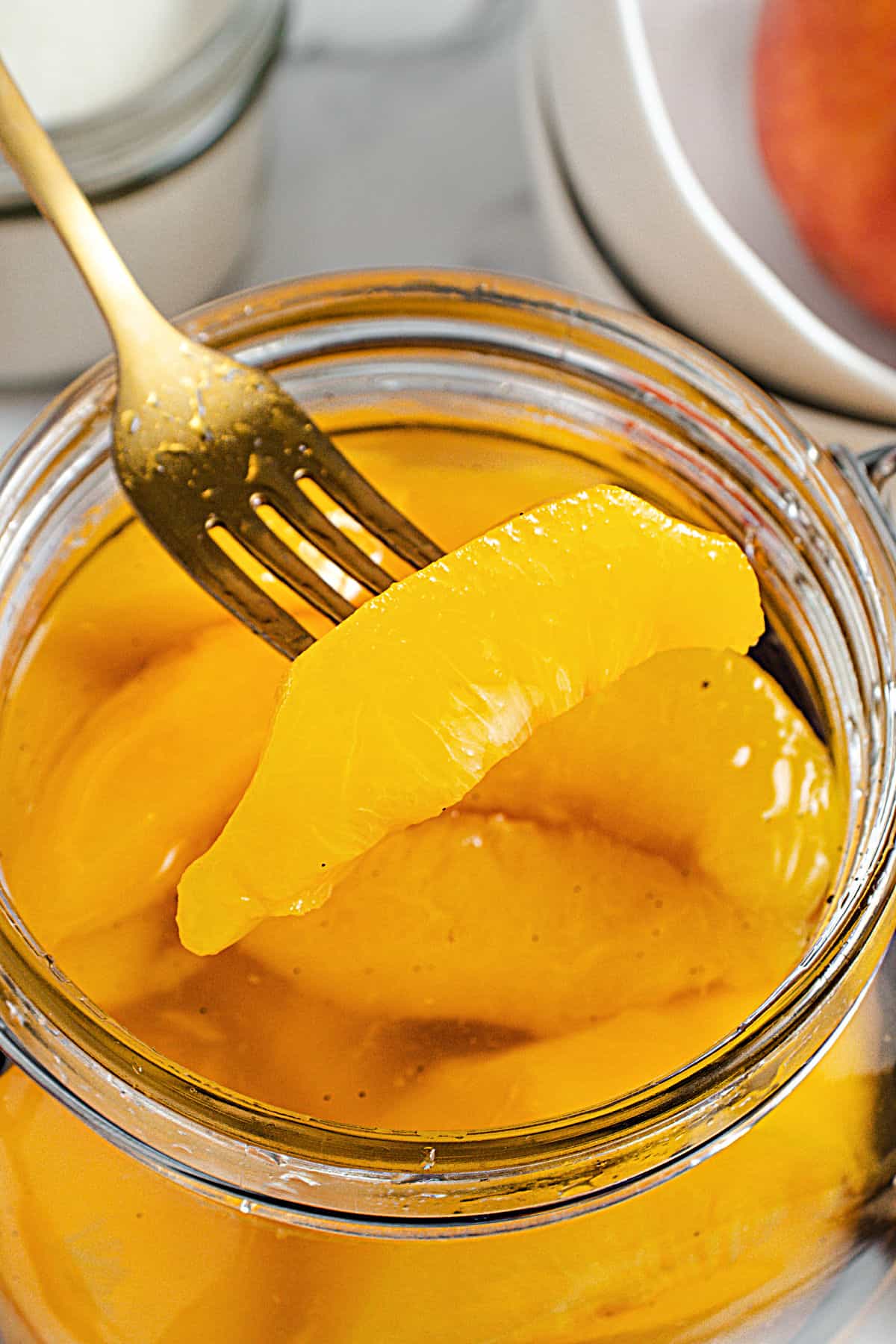 Forked piece of peach from jar with more slices in syrup.