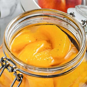 Sliced cooked peaches in syrup in an opened mason jar.
