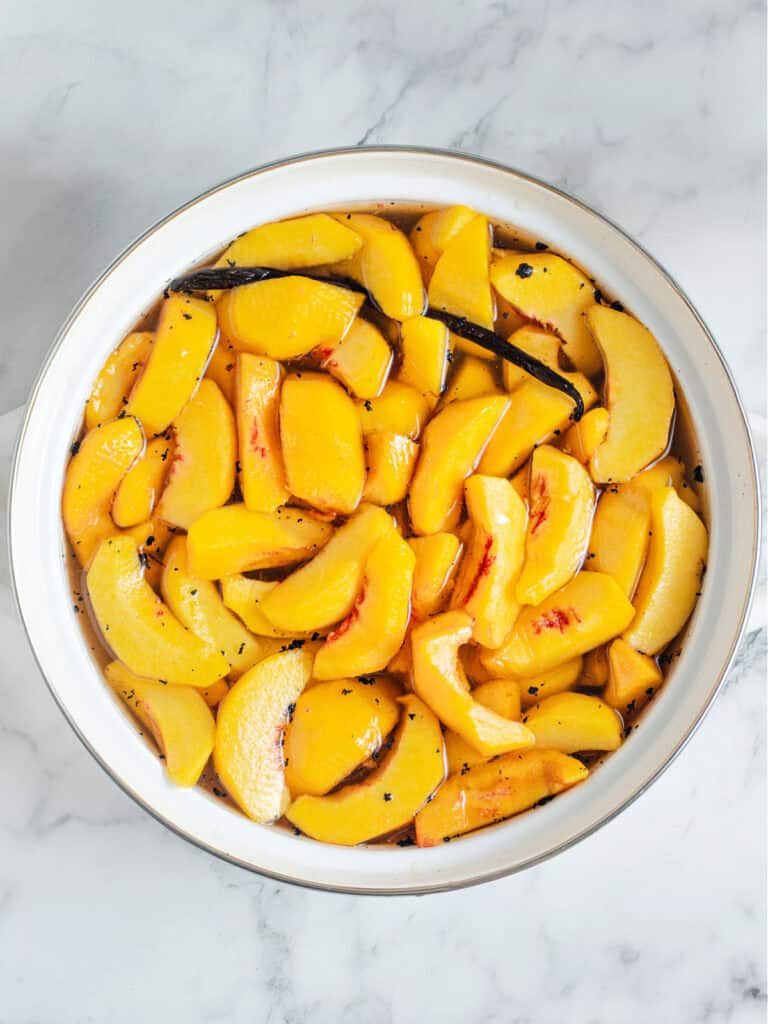 Vanilla syrup with fresh peach slices in a white saucepan. Gray background, top view.