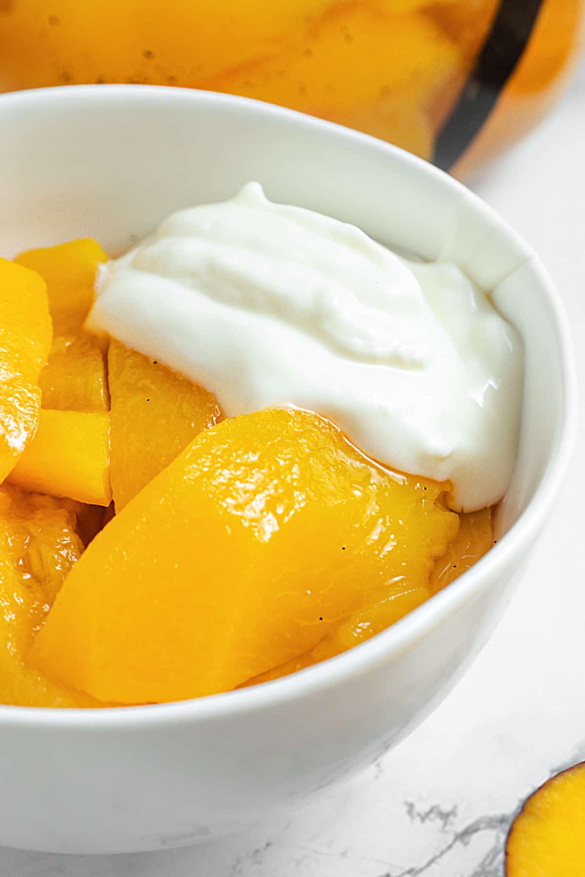 White bowl with sliced peaches, syrup and yogurt. Partial view.