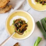 Close up white bowl with potato soup with mushroom garnish. White marbled surface.
