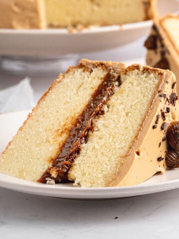 Slice of vanilla dulce de leche cake on a white plate. More cake in the background.