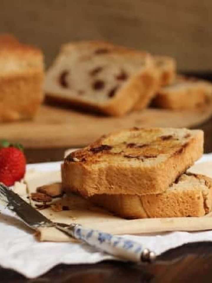 Stack of cinnamon bread toast on dark surface with white napkins, a butter knife, whole bread in the background.