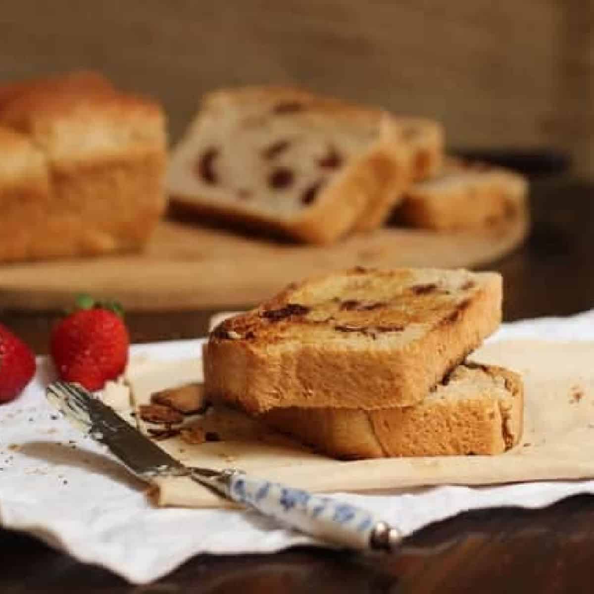 Slices of cinnamon bread on white cloth, dark surface, a butter knife, whole bread in the background.
