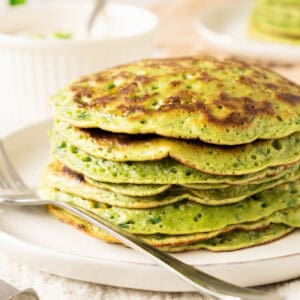 Chard pancakes in a stack on a white plate. A silver fork, white bowl.