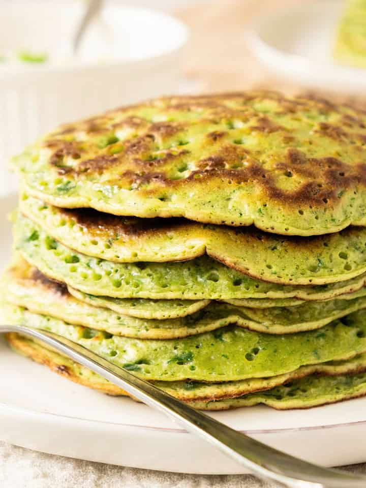 Chard pancakes in a stack on a white plate. A silver fork, white bowl.