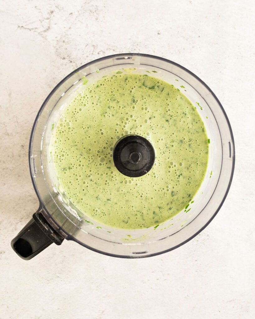 Pancake batter with green chard in the bowl of a food processor. Top view. Stone background.