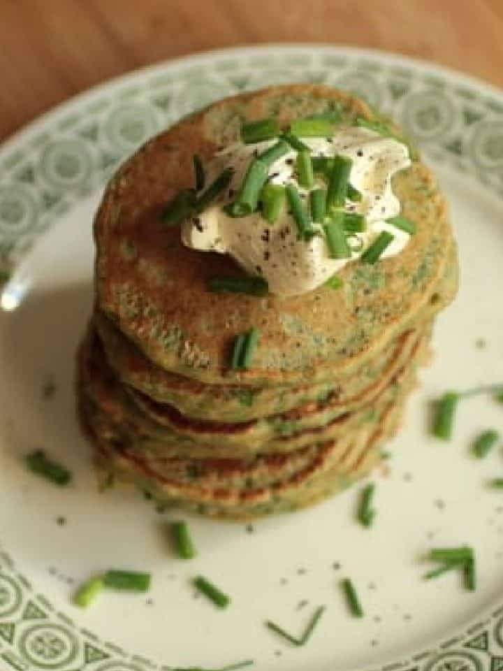 Tall stack of small chard pancakes on a plate. Dollop of cream on top.