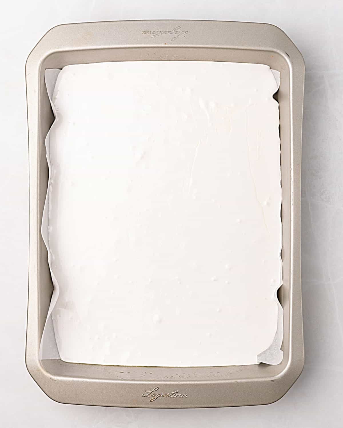 Marshmallow mixture in a rectangular pan on a white surface.