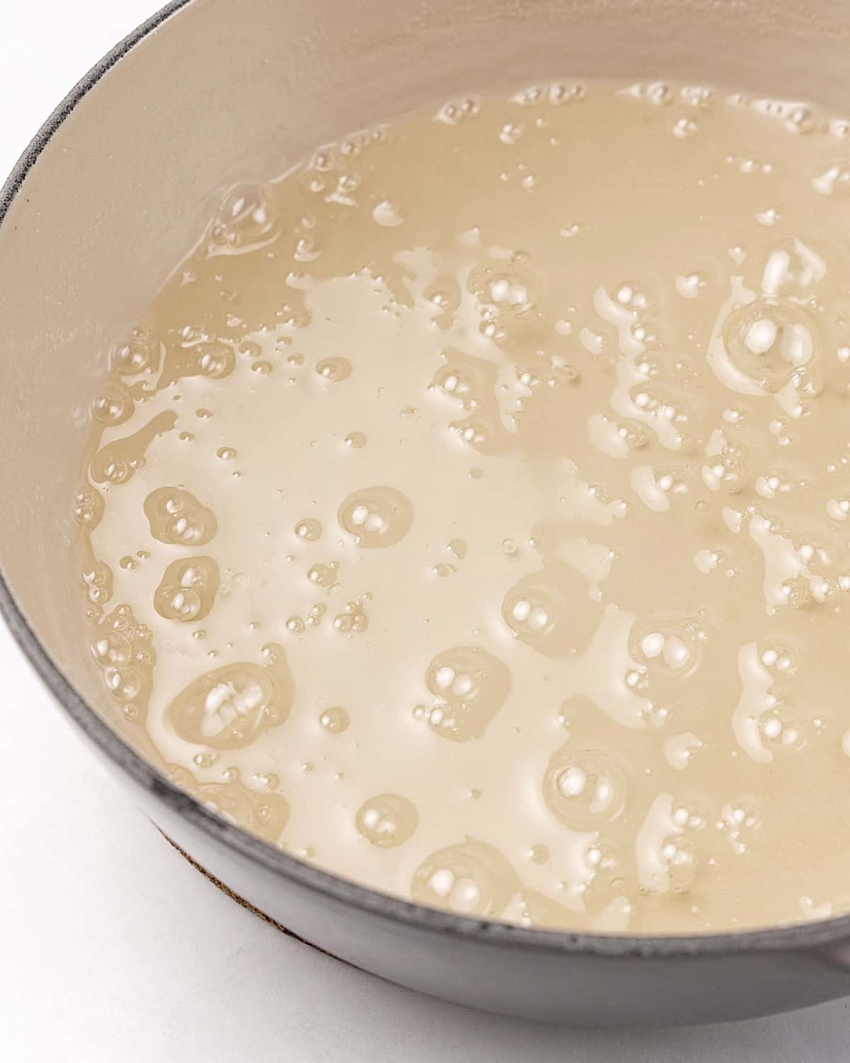 Syrup bubbling in a cream-colored skillet. White surface.