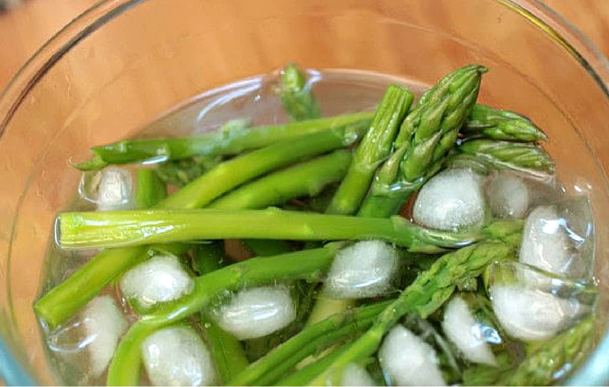 Ice water in a glass bowl with green asparagus stalks.