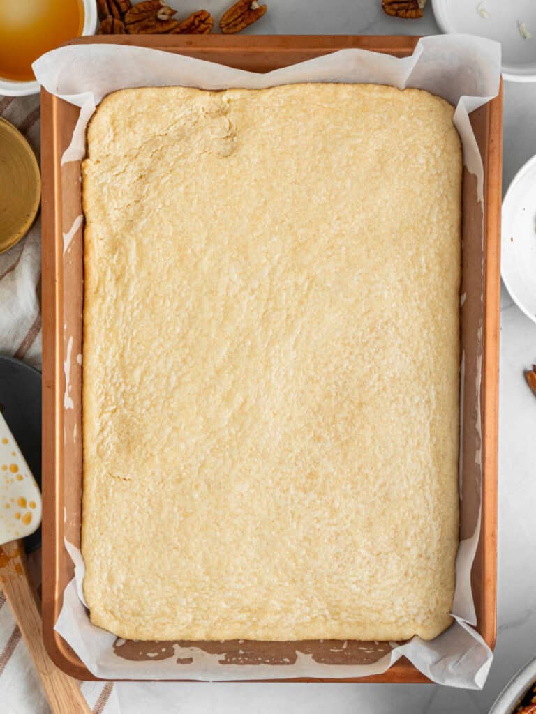 Prebaked shortbread crust in a rectangular copper baking pan with parchment. Top view.