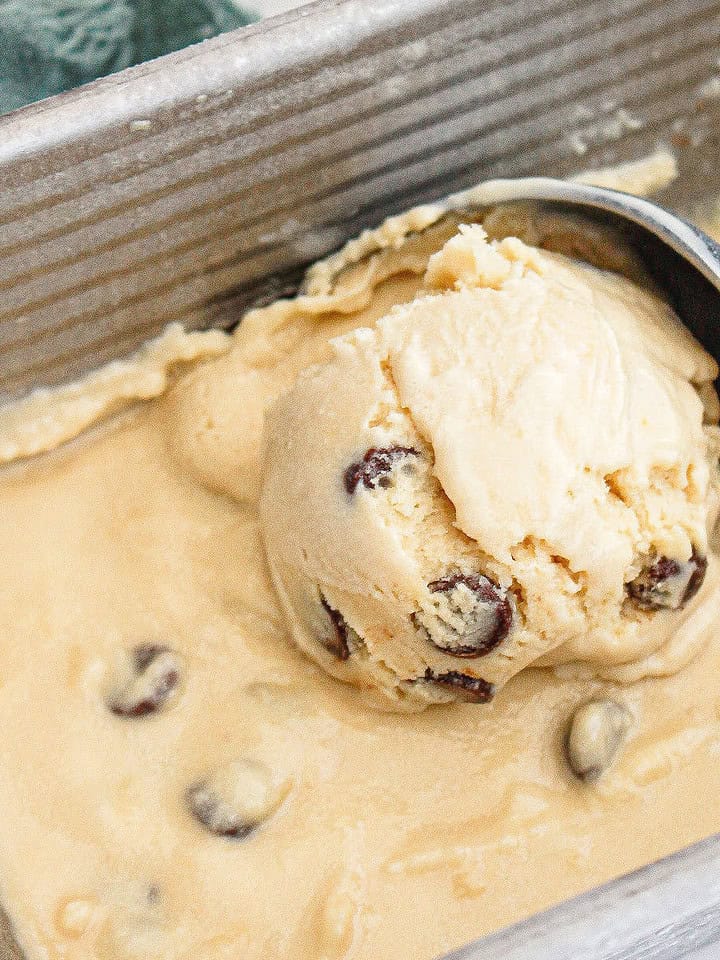 Close up image scooping chocolate chip cookie ice cream from a metal pan.