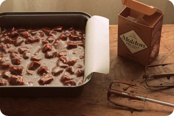 Square pan with fudge and Maldon salt package on a wooden table.