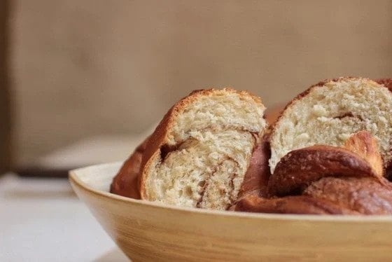 Pieces of cinnamon challah bread in a yellow wood container. Beige background. 