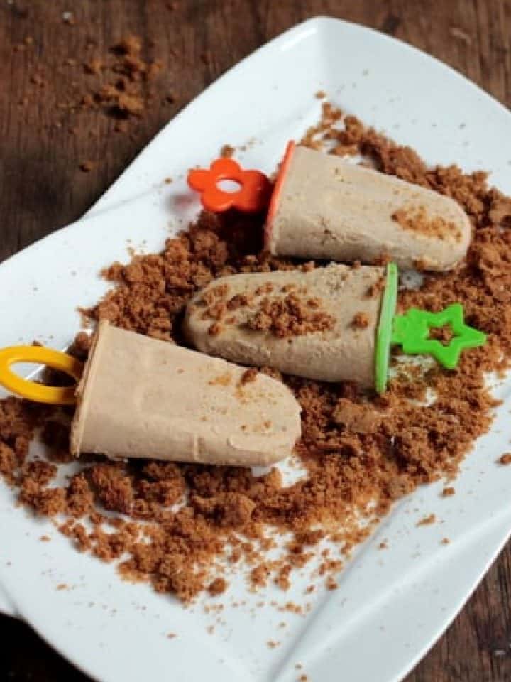 A white plate with three cinnamon popsicles with colorful handles. Wooden surface.