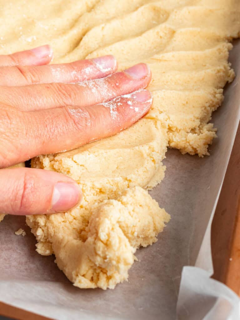 Patting dough for pecan bars on a parchment-lined pan.